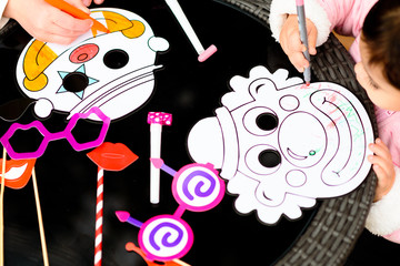 Happy children draw with pencils clown mask. Close up of hands little boy and girl sitting at the table near Party accessory's and painting. Purim, Halloween, birthday concept.