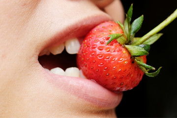 Young woman is eating fresh strawberry.