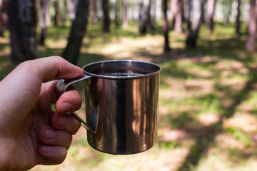 male traveler holding a mug of tea in the forest