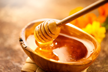 Honey. Healthy organic thick honey dripping from the honey dipper in wooden bowl. Sweet dessert...