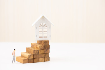 Miniature people small figure walking to model white house on wood block stacking step stair. Property investment and house mortgage financial concept, Home protect, Insurance. With copy space.