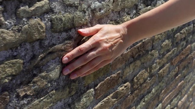 Woman sliding hand against old ancient red brick wall in slow motion. Female hand touching hard rough surface of stone bridge