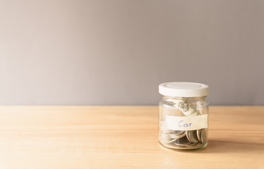 Coin in a glass jar on wooden desk with copy space, Saving money for buy a car concept