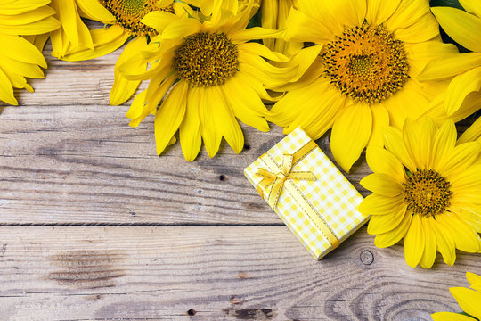 Background with a bouquet of yellow sunflowers and gift box on a old wooden table.