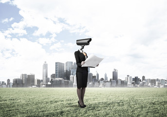 Camera headed woman standing on green grass against modern citys
