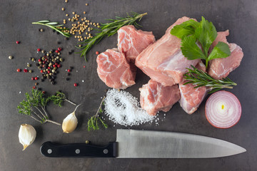 Fresh raw meat with herbs, spices and a butcher knife lies on the surface of a dark stone. Cooking concept.