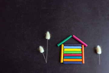 Bright pastel crayons are arranged in the shape of a house on a black school slate. Children's creativity. Concept- sweet home, back to school, mortgage, your new home.