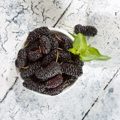 Fresh mulberries in a bowl on the table, top view.