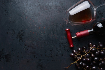 Glass with red wine,  bottle with corkscrew and red grape clusters on black rustic background, top view. Place for your design, text, article, advertisement or product. Red wine concept