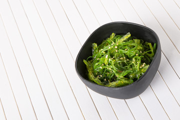 Salad of green algae in a black bowl on a white background. Copyspace