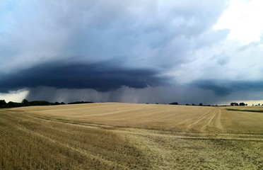Dramatischer Himmel mit Unwetter über abgeerntetem Stoppelfeld Weizen, Panorama