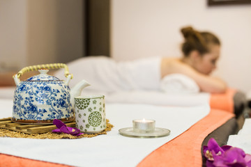 Young beautiful girl in spa salon. The girl lies on the couch for a massage after a rejuvenation procedure. a composition in Thai style with an orchid and a teapot with green tea