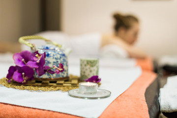 Young beautiful girl in spa salon. The girl lies on the couch for a massage after a rejuvenation procedure. a composition in Thai style with an orchid and a teapot with green tea