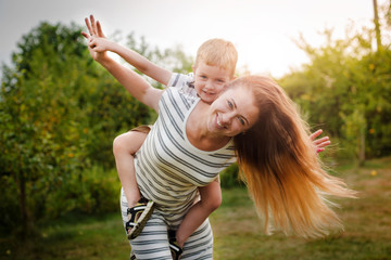 Happy Caucasian mother and son outdoors in park on sunny spring day. Young brunette mother lifting her son in park having fun enjoying motherhood. Square, retouched.