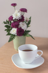 Vase with flowers and a cup of black tea on the table.
