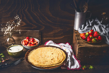 Homemade crepes on dark rustic kitchen table with strawberries and yogurt in bowls . Country style...