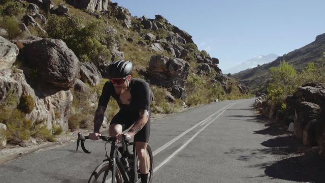 Video of a tough male bicycle rider climing up the mountain road and drinking water to stay hydrated. Cyclist practising hard for his race outdoors.
