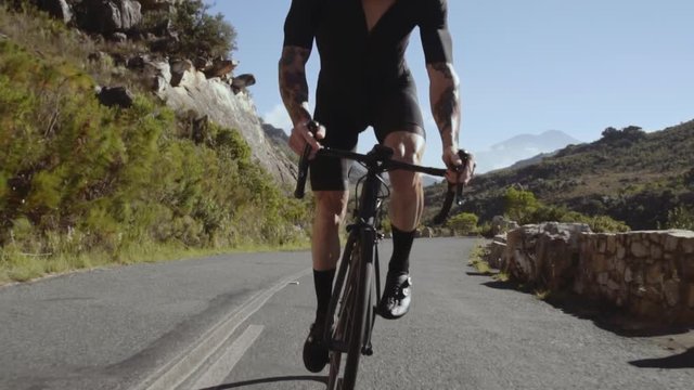 Tracking shot of a fit male cyclist sprinting while doing uphill a bike. Sportsman climbing up the curvy mountain road on a bicycle. 