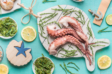 Octopus tentacles served on white cutting board in fish shape with seaweeds salad in bowls on light blue table background, top view. Seafood cooking concept © VICUSCHKA