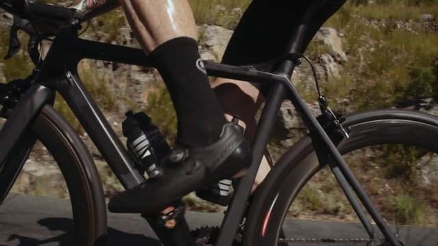 Close up of strong and muscular sportsman legs pedaling the cycle uphill. Focus on muscular legs of professional cyclist.