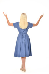 Fototapeta premium full length portrait of blonde girl wearing blue dress. standing pose with back to the camera. isolated on white studio background.