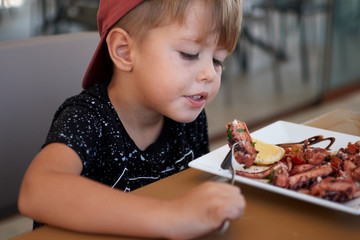 Little boy eating grilled octopus