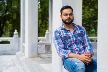 Fototapeta premium Portrait Of Young Handsome Indian Man In Park Sitting