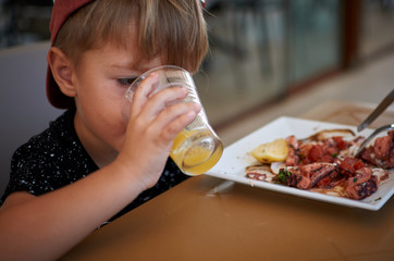 Little boy eating healthy Mediterranean food - octopus and orange juice