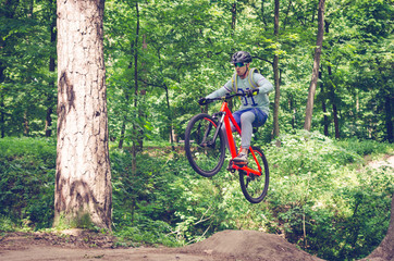Fototapeta na wymiar Cyclist in helmet on an orange bike doing a trick in a springboard jump in the forest, motion blur