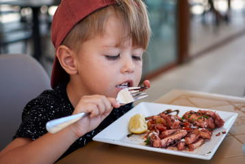 Little boy looking for tasty octopus on his fork