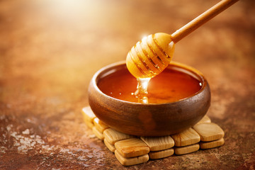 Honey. Healthy organic thick honey dripping from the honey dipper in wooden bowl. Sweet dessert...