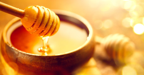 Honey. Healthy organic thick honey dripping from the honey dipper in wooden bowl. Sweet dessert...