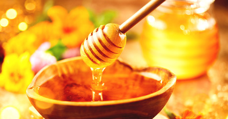 Honey. Healthy organic thick honey dripping from the honey dipper in wooden bowl. Sweet dessert...