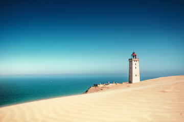 Bright beach sand dunes with the famous danish landmark lighthouse with blue sky background....