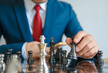 Retro style image of a businessman with clasped hands planning strategy with chess figures on an old wooden table.