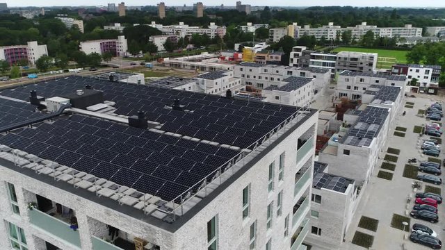 Aerial of modern apartment building roof filled with photovoltaic solar panels which absorb sunlight as source of energy to generate electricity also showing more living buildings in background 4k
