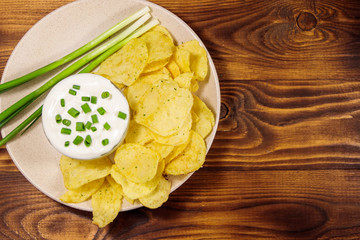 Crispy potato chips with green onion and sour cream on wooden table. Top view