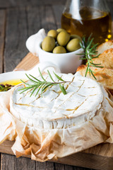 Baked camembert cheese. Fresh Brie cheese and a slice on a wooden board with nuts, honey, rosemary, baguette bread grilled toasts and leaves. Brie type of cheese. Italian, French cheese.