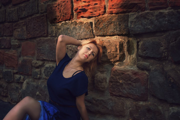 Young beautiful woman in a blue dress posing near an old textured stone wall.