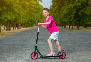 In the summer in the park the boy rolls on rollers and the girl rolls on a scooter