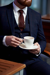 Business style. Men style. Businessman in a blue jacket with a cup of coffee in the cafe at the table, close-up