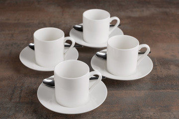 Fototapeta na wymiar four white empty cups on saucers, four spoons, on a brown table, a concept of nutrition
