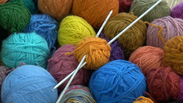 Rotating many colorful yarn wool balls with two metal knitting needles

