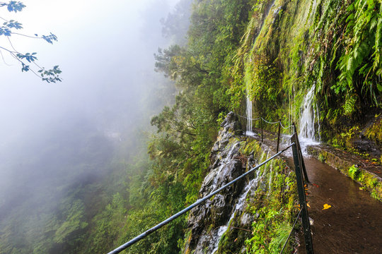 Fototapeta Waterfall falling on the walking trail along a levada in the mountains of Madeira, Portugal
