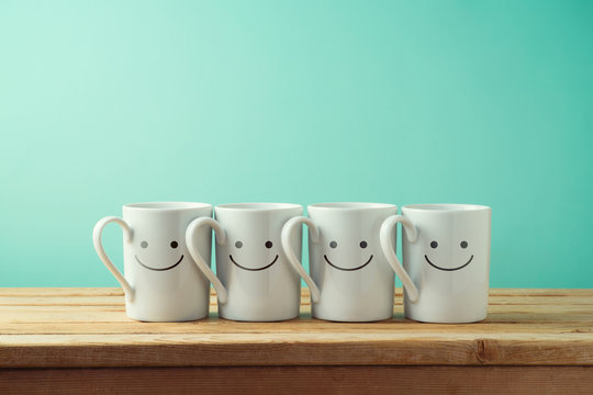 Coffee cups with funny faces on wooden table