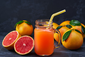 Obraz na płótnie Canvas Glass jar of fresh grapefruit juice with fresh fruits on dark table.
