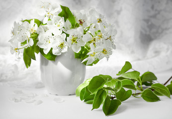 Bunch of white flowers and a branch of a pear tree in front of folds of a wedding dress