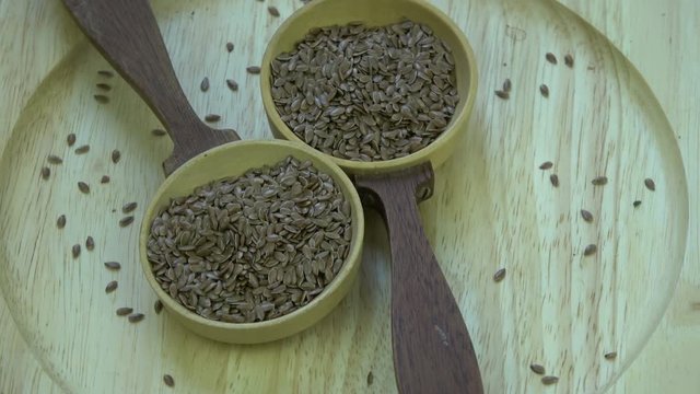 Rotating  two wooden spoons with flax seeds on wooden plate 