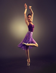 Ballerina. Young graceful woman ballet dancer, dressed in professional outfit, shoes and violet weightless skirt is demonstrating dancing skill. Beauty of classic ballet dance. 
