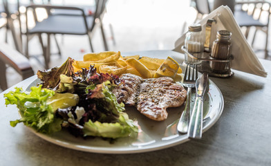 Grilled chicken fillet with fried potato, Iceberg salad and vegetables on a table in a Mediterranean restaurant